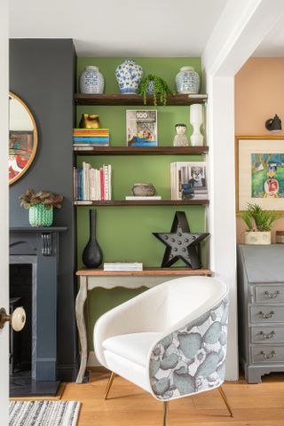 Green painted alcoves with wooden shelving and desk, black painted fireplace and white and green pattern armchair