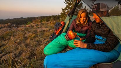 Best sleeping bag: Man and woman sitting in open tent in their Kelty Cosmic Ultra 20F sleeping bags