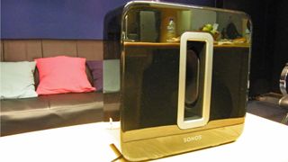 En Sonos Sub som skiftar i svart och guld står på ett vitt vardagsrumsbord.