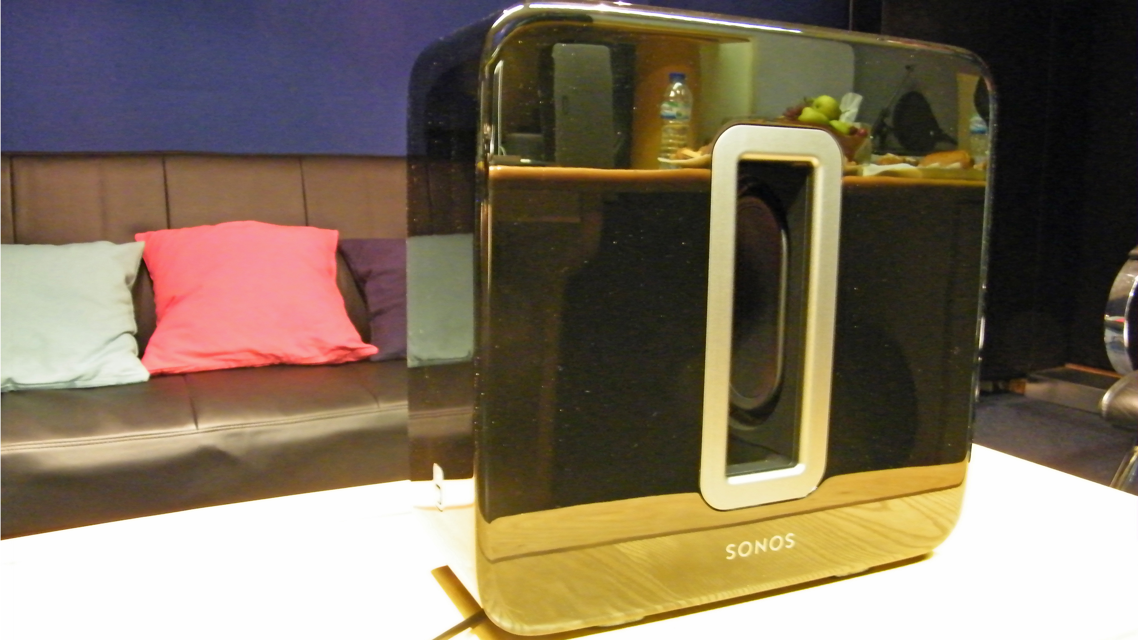 En Sonos Sub som skiftar i svart och guld står på ett vitt vardagsrumsbord.