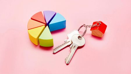 Pie chart made of colorful building blocks and keys with a small house keyring on pink background 