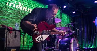Jim Babjak of the Smithereens crouches onstage with his red Rickenbacker. The stage is lit in green.