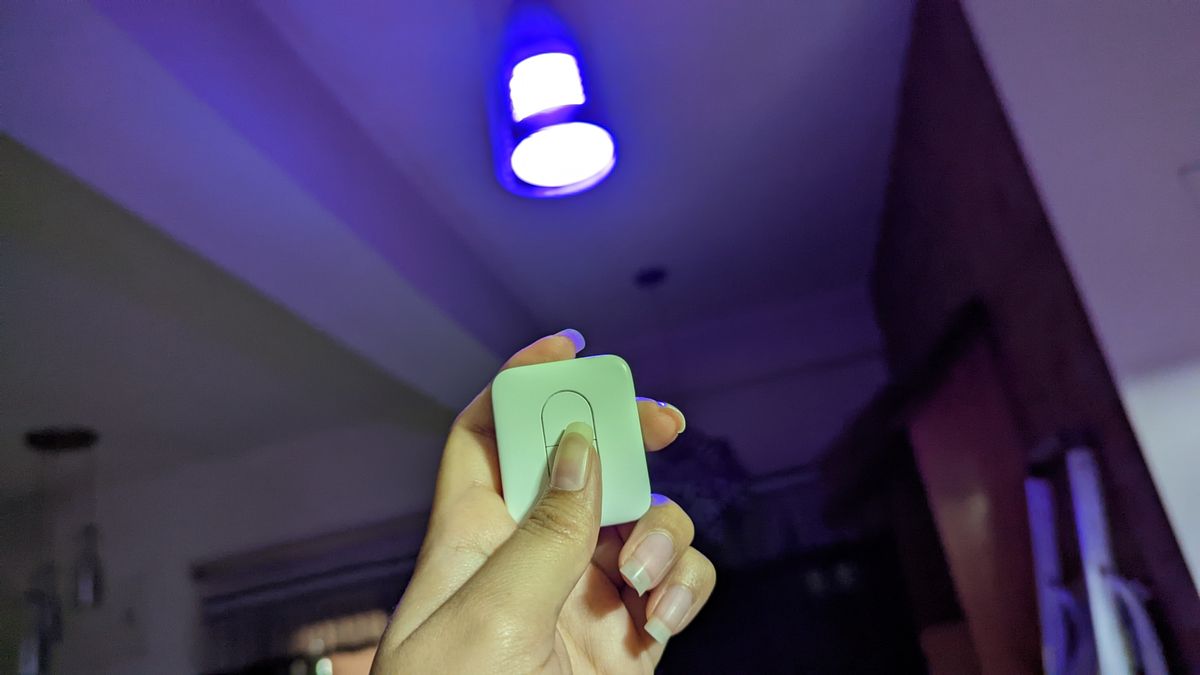 SwitchBot smart remote held up in one hand, pointing at a SwitchBot smart color light bulb installed in a light fixture