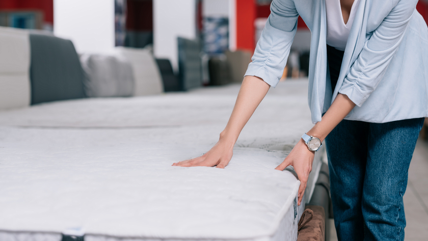 A woman feeling the side and top of a mattress as she shops