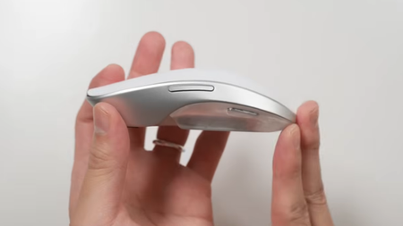 Two hands hold a prototype of the smooth, wireless Melt Mouse aloft on a white background.