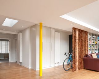 Basement living space with skylights, yellow steel structure, recessed ceiling, paneled wood screen, wooden flooring