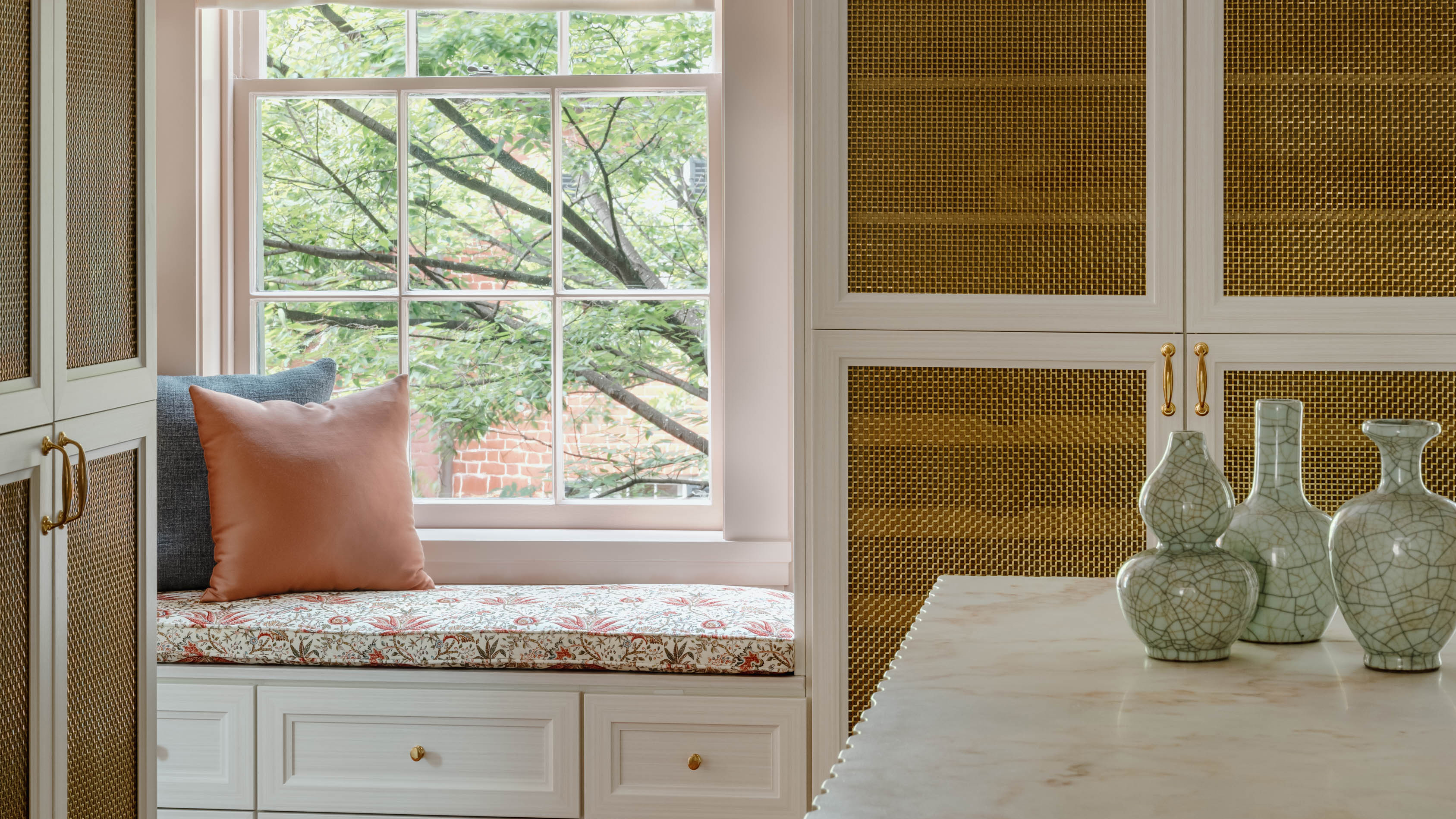 window seat with upholstered pillows in soft pinks and with vases on the surface in the foreground