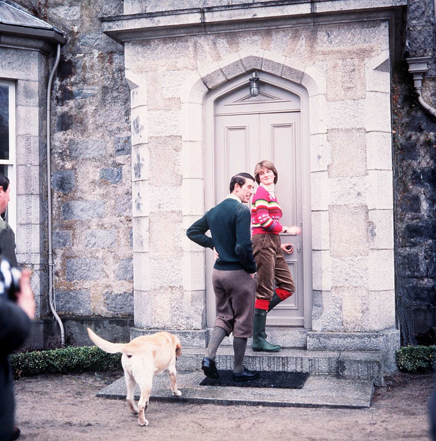 Princess Diana and Prince Charles walking into a door at Balmoral in 1981 wearing boots with a dog behind them
