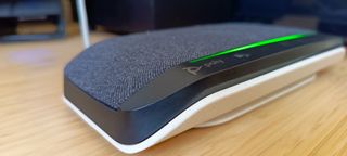 A grey, black and white Poly Sync 10 speakerphone sitting on a brown wooden desk