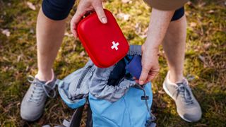 Person taking first aid kit out of backpack outdoors