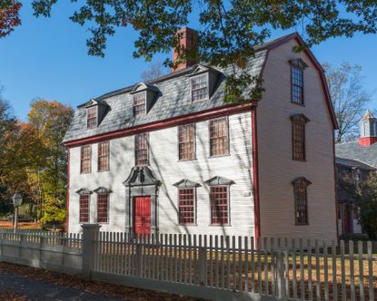 exterior of white wooden Dutch style colonial home with gambrel roof and red front door