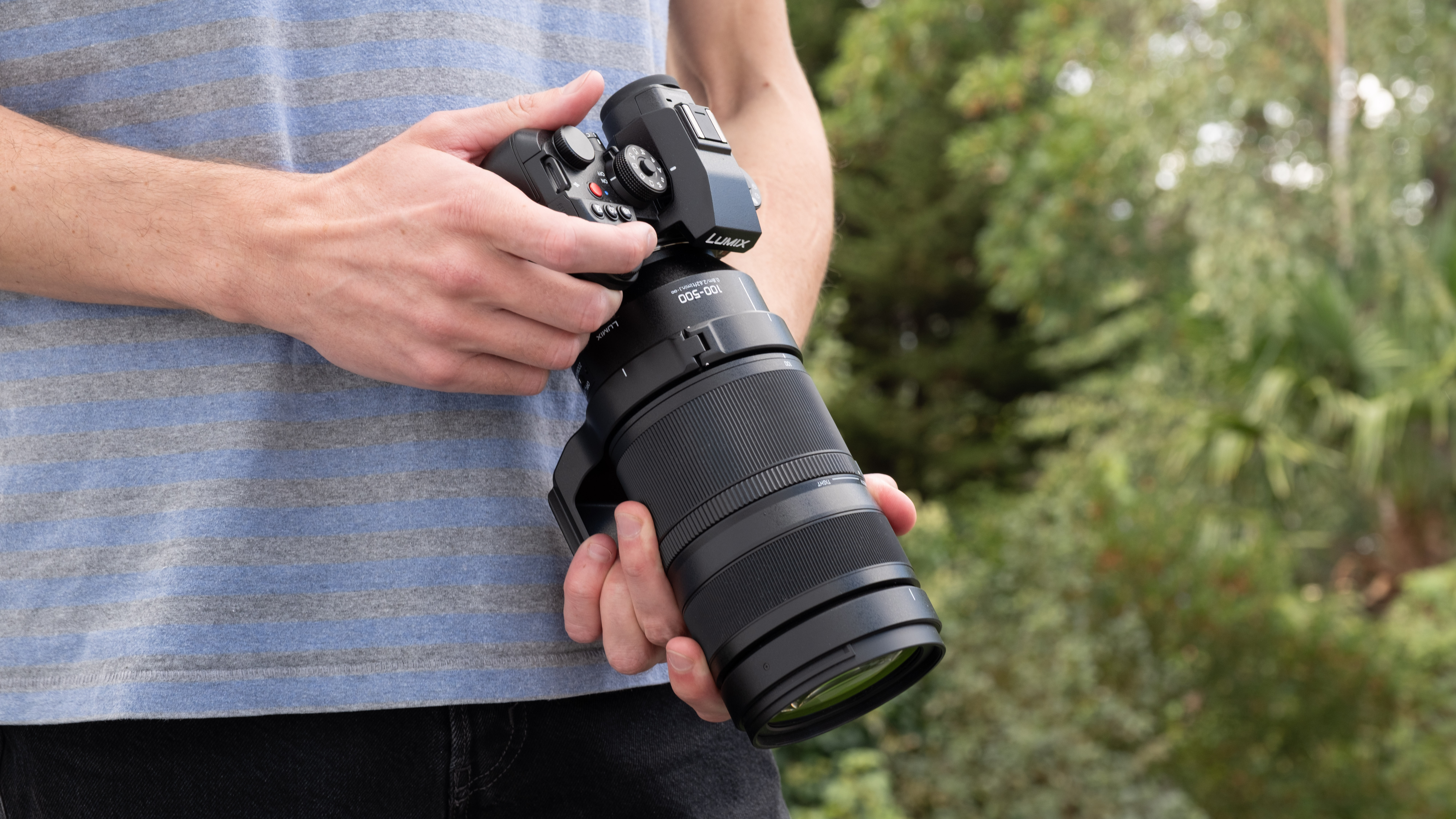 Panasonic Lumix S1II camera with a Lumix S 100-500mm f/5-7.1 lens attached held in a pair of hands outdoors