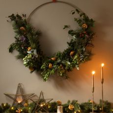 A large modern Christmas wreath hung on the wall above a decorated fireplace mantelpiece