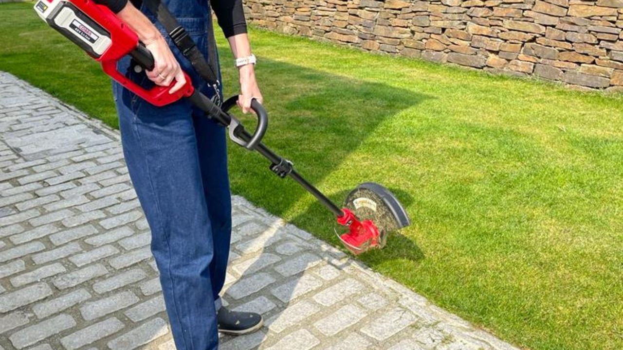 Cobra GT3240VZ grass trimmer in use on green grass with person holding in blue dungarees