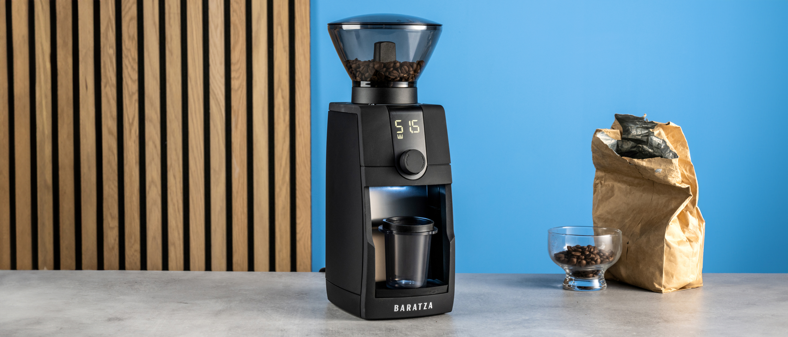 the baratza encore esp pro coffee grinder photographed against a blue tom's guide background with a bag of coffee to the side and showing the grinder in action