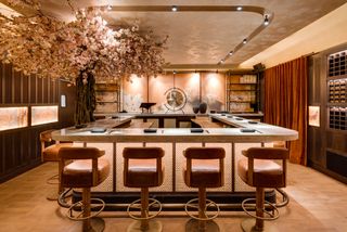 The Japanese-inspired interiors of a restaurant feature a mix of mid-century modern and Asian furniture, and a live cherry plant, in a warm setting.