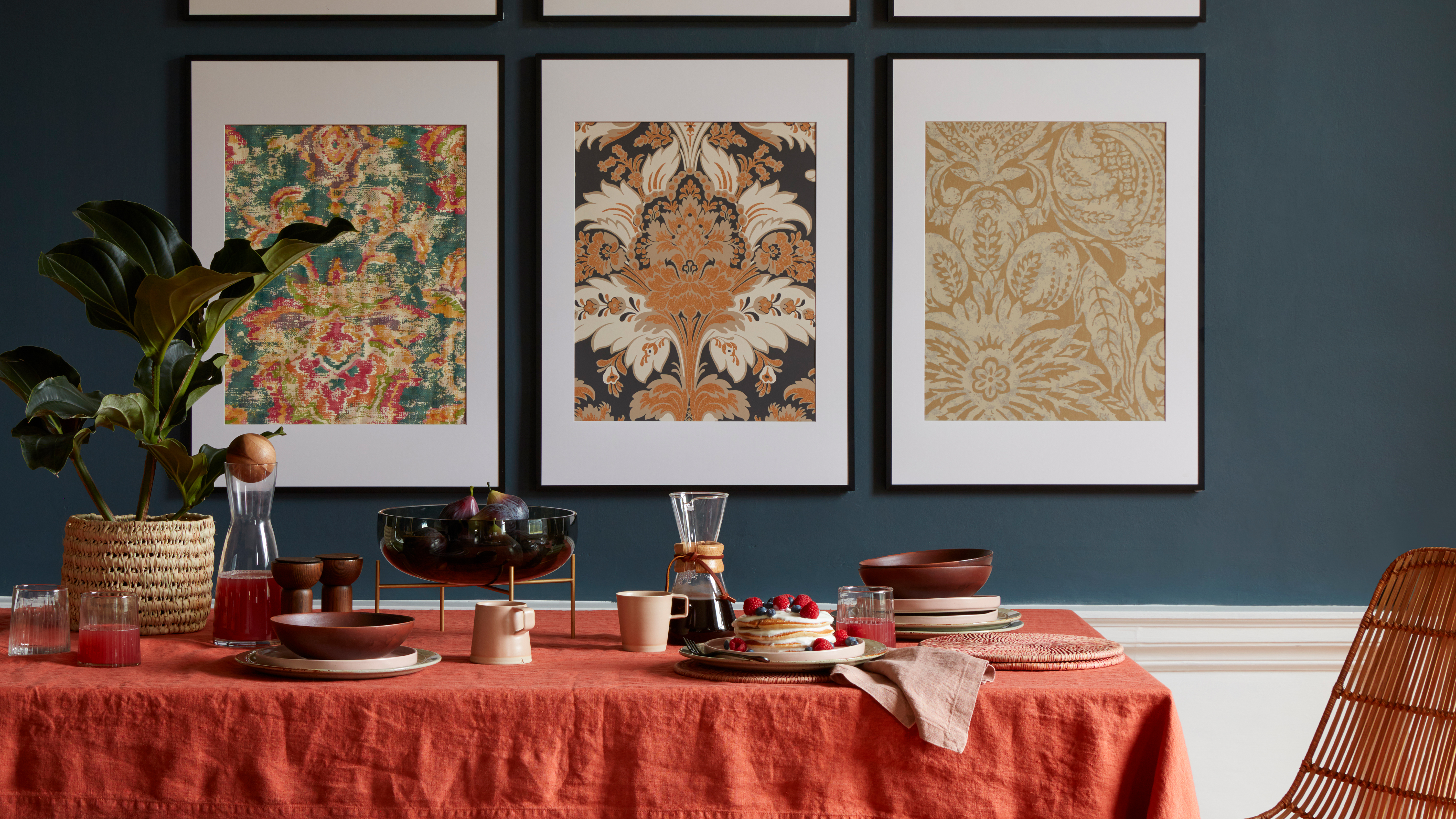 Dining room with dark blue wall and framed William Morris wall art, and a table dressed with an orange linen tablecloth