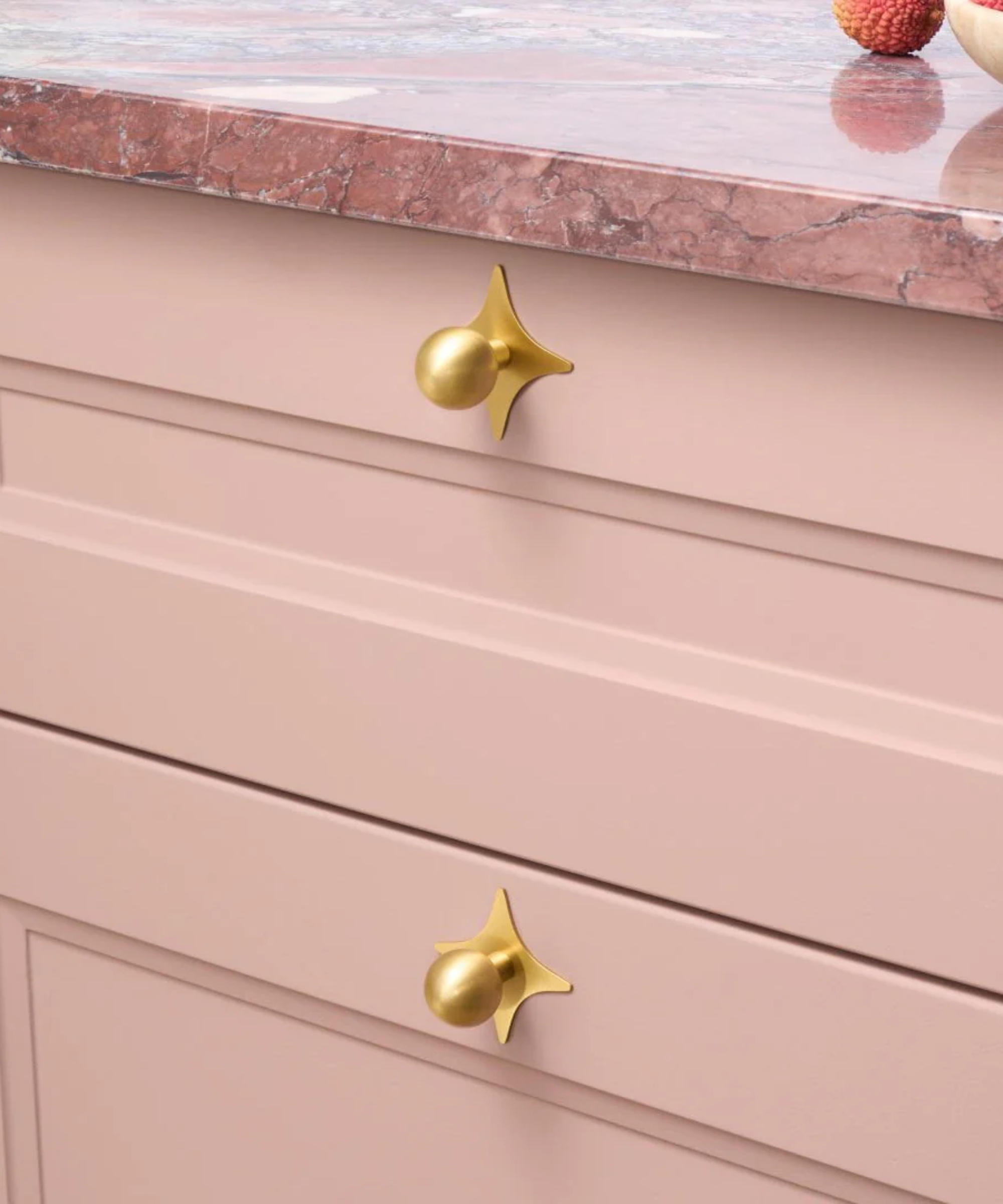 gold drawer knobs with star shaped back plate on pink drawers with pink marble top