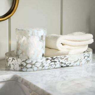 A glass counter tray with a matching pot and a folded face cloth on top. 