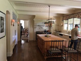 a tired kitchen before its remodel, with oak island and floral curtains