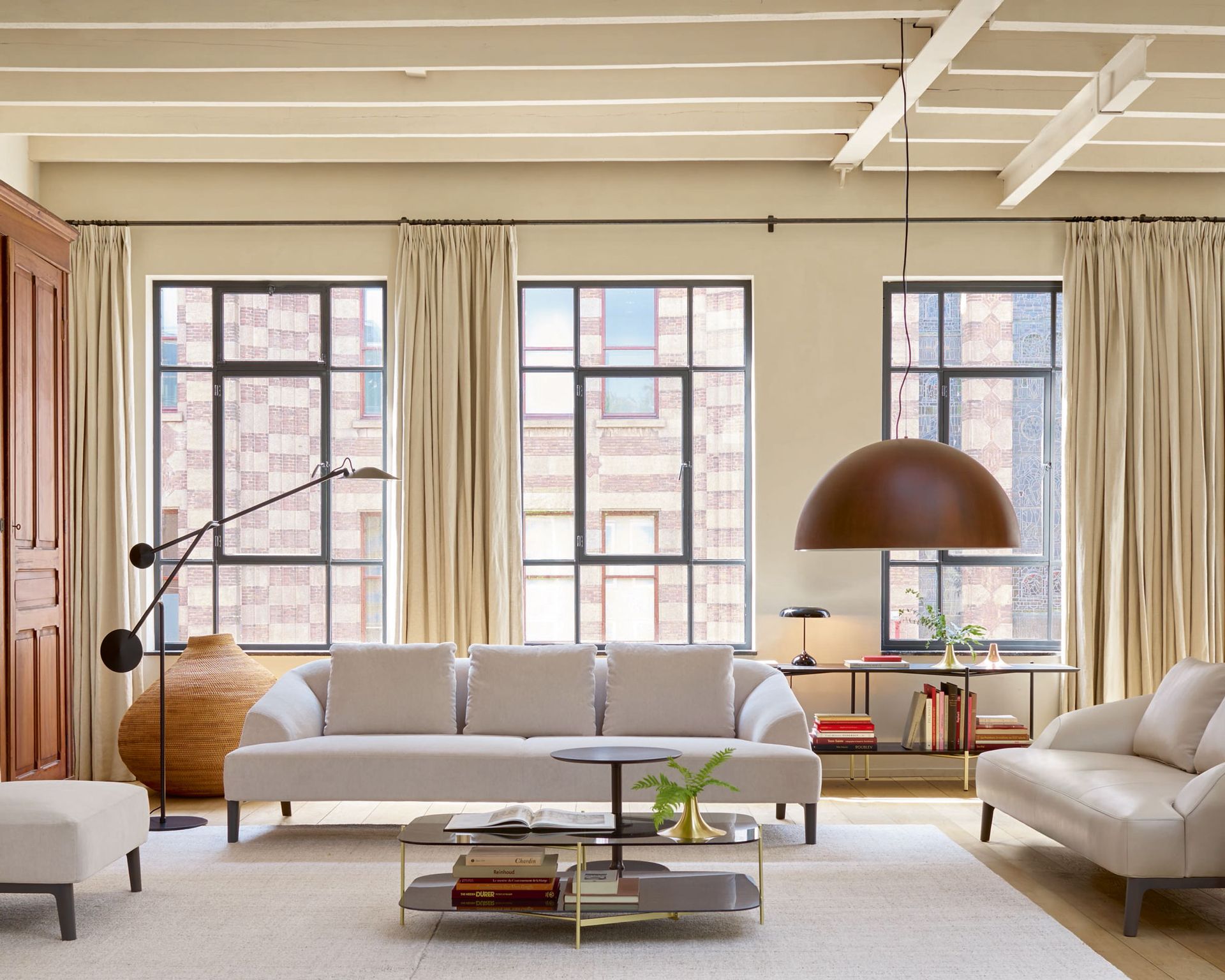 An example of how to plan living room lighting, with white sofas, black floor lamps and a large pendant light in front of three large windows.