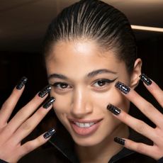 Model with square nails holding their nails up in front of their face.