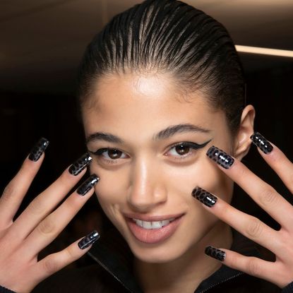 Model with square nails holding their nails up in front of their face.