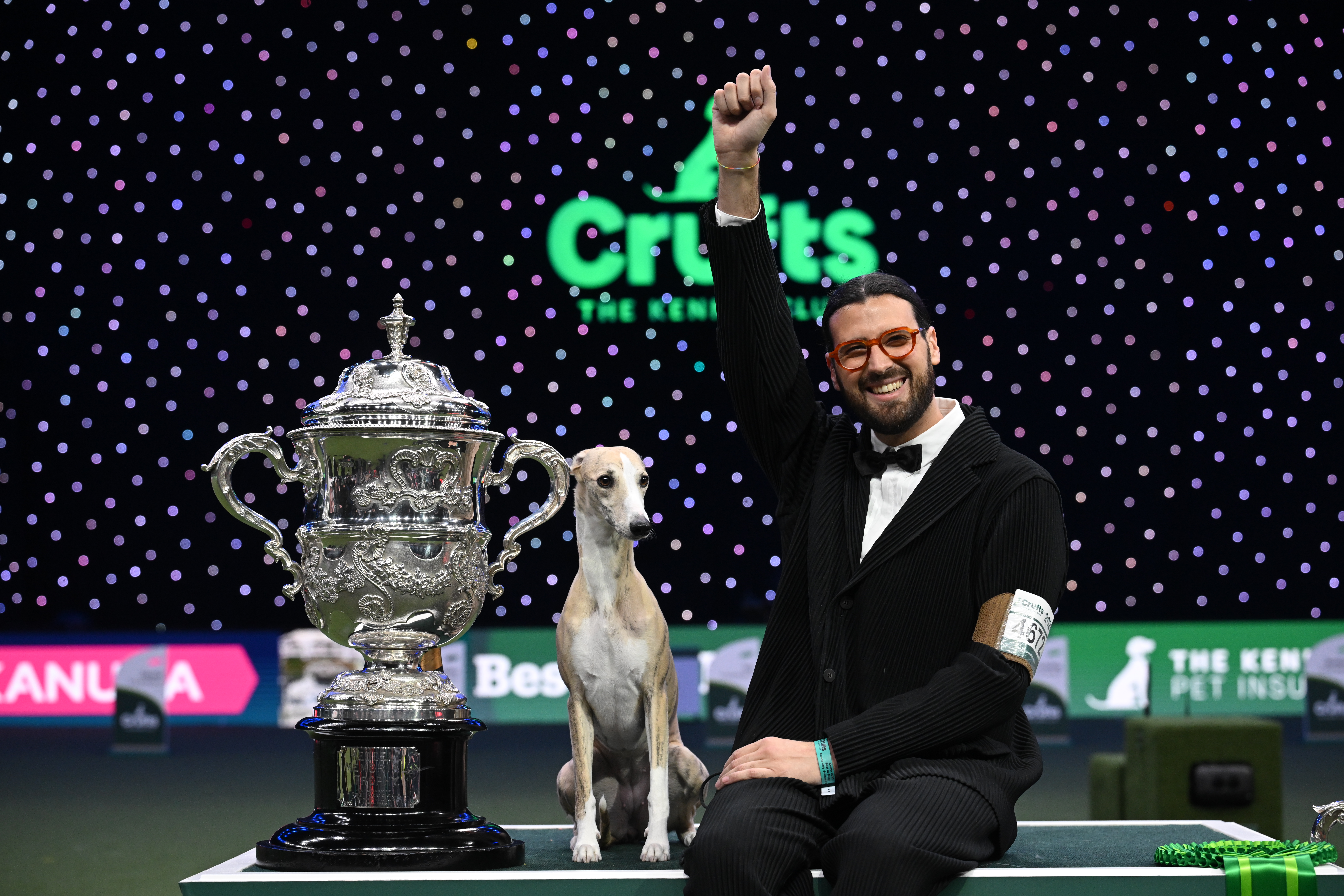 Handler Enrico De Gaspari celebrates beside whippet Una Donna Che Conta and the Crufts Best in Show trophy at the NEC in Birmingham, March 2025.