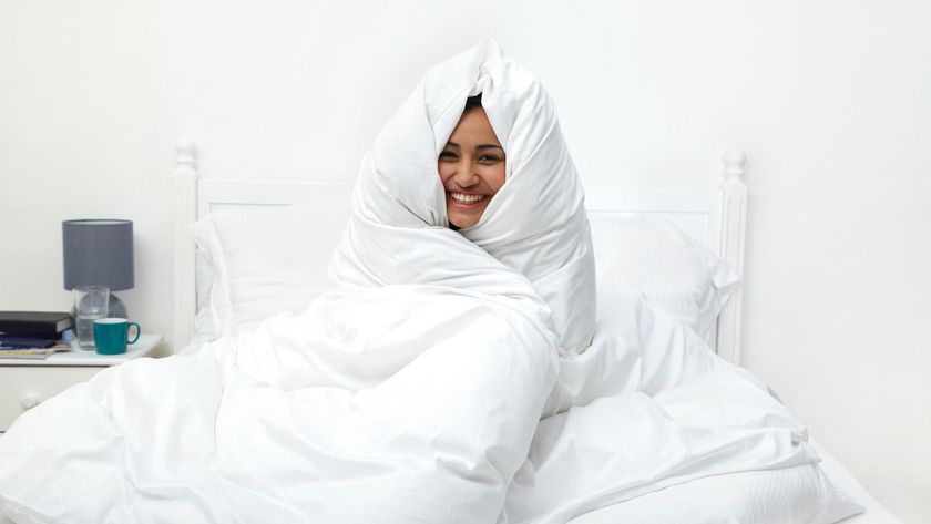 A woman wrapped up in a white duvet sat on her bed smiling and laughing