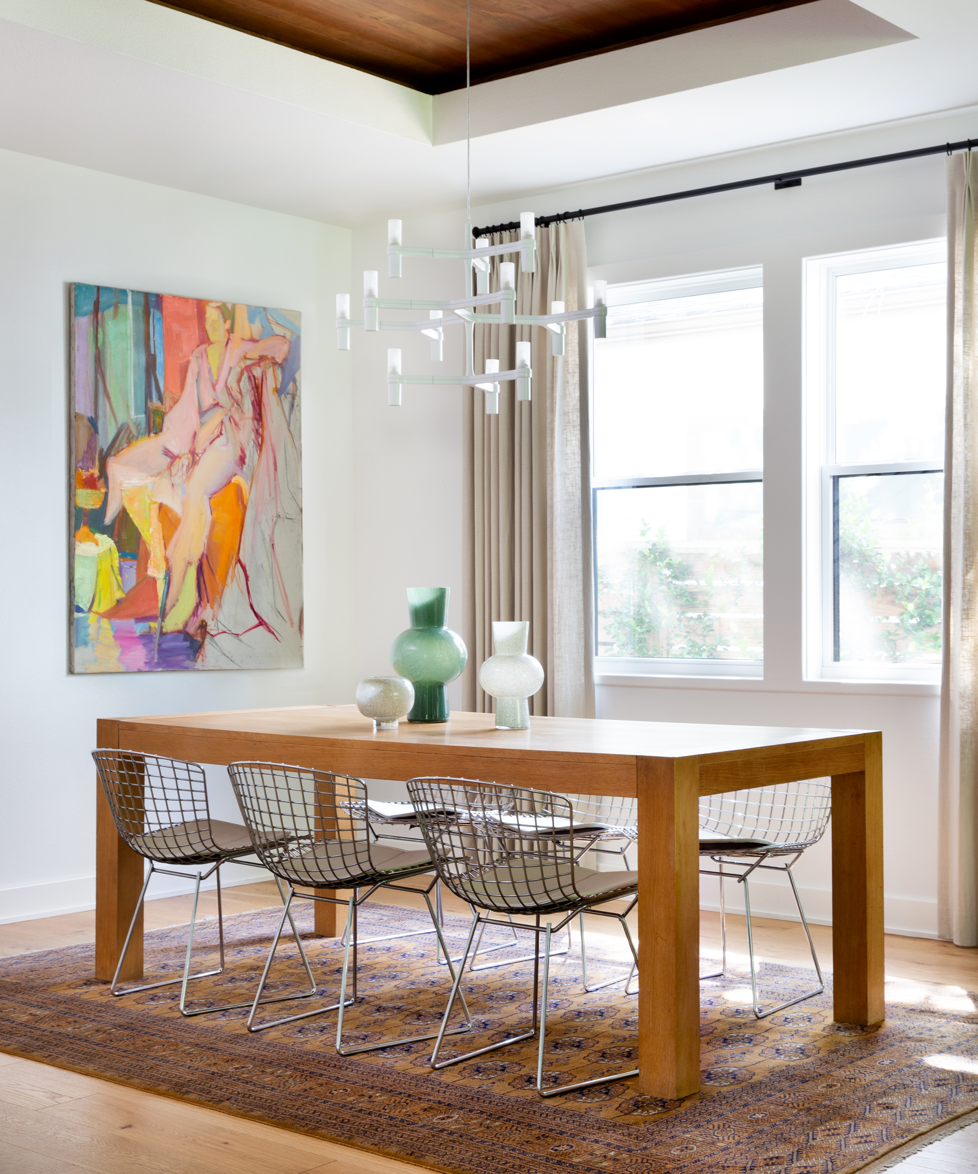 A dining room idea with a large wooden table, basket metal chairs, abstract art and a contemporary candle chandelier