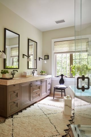neutral bathroom farmhouse style with textured rug, walnut double vanity, black faucets, black matching mirrors, wall lights, bath tub, shower on right, marble stool