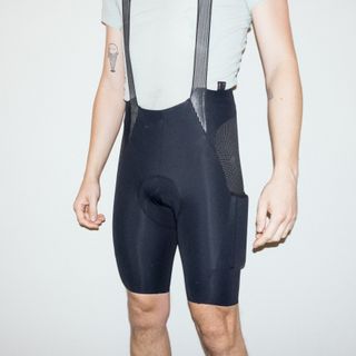 A white man wears a set of cargo bib shorts against a white background