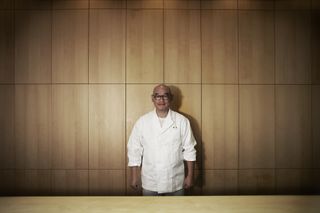 View of The Araki restaurant chef and founder Mitsuhiro Araki wearing a white chef jacket standing in front of a wood panelled wall