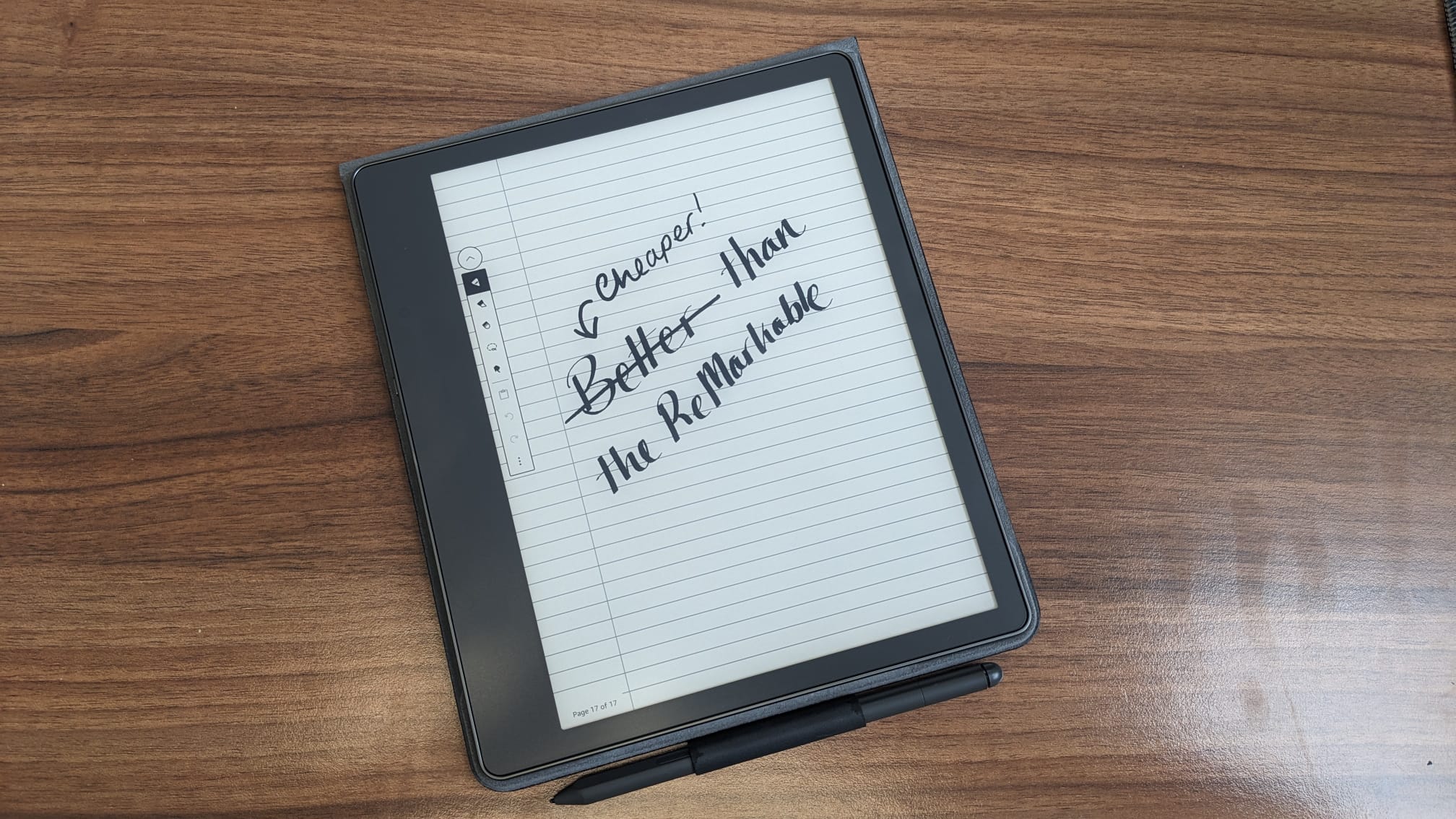 The Kindle Scribe on a woodgrain desk, with writing on the display that says "cheaper than the reMarkable"