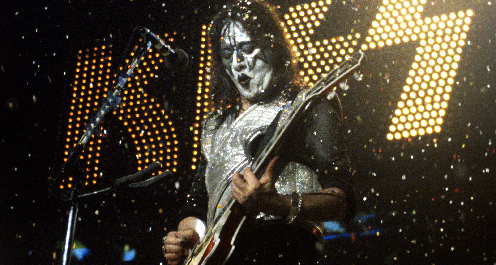 Ace Frehley of Kiss performs in 1996 with confetti filling the air and the band's logo in lights