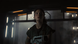 a woman holds a futuristic rifle inside a dark, foggy corridor