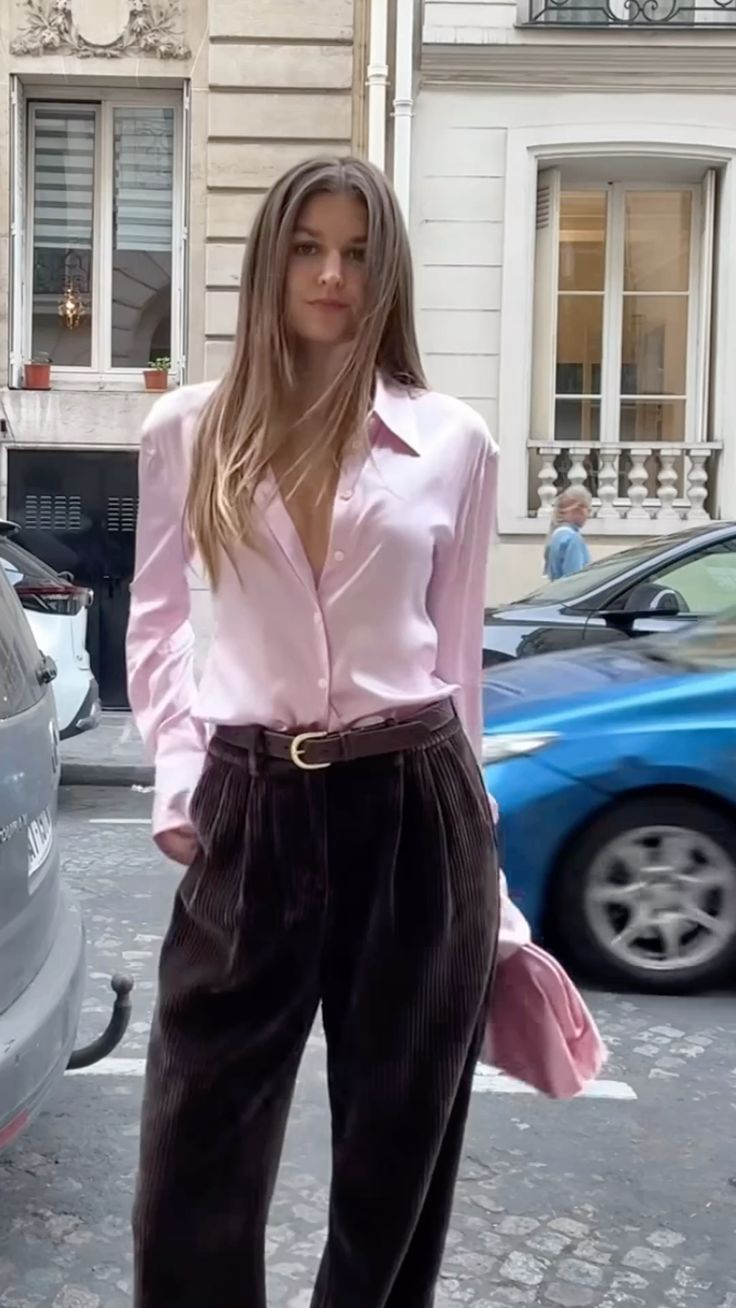 Woman wearing a pink satin shirt tucked into chocolate brown trousers.