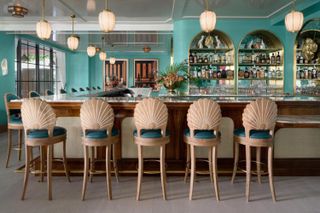A row of scalloped back bar stools facing a green bar with arched shelves and art deco pendant lights above