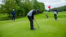 Neil Tappin hitting a putt on the green, watched by Barry Plummer and Dan Parker, at Burhill Golf Club