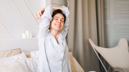 Woman doing 5-minute morning stretching routine in bed, smiling in pyjamas