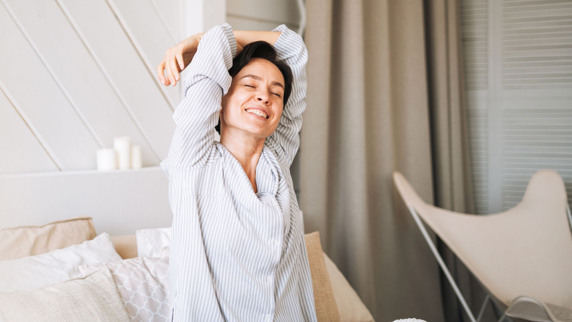 Woman doing 5-minute morning stretching routine in bed, smiling in pyjamas