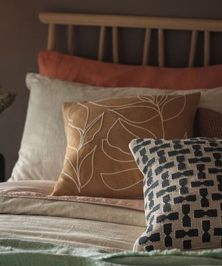 Close up of cozy bed with cream, pink and orange bedding, leaf outlined cushions, patterned cushion