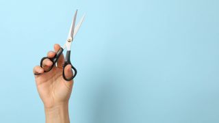 A hand holding up a pair of scissors on a blue background