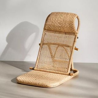A wicker floor chair with a curved head pillow