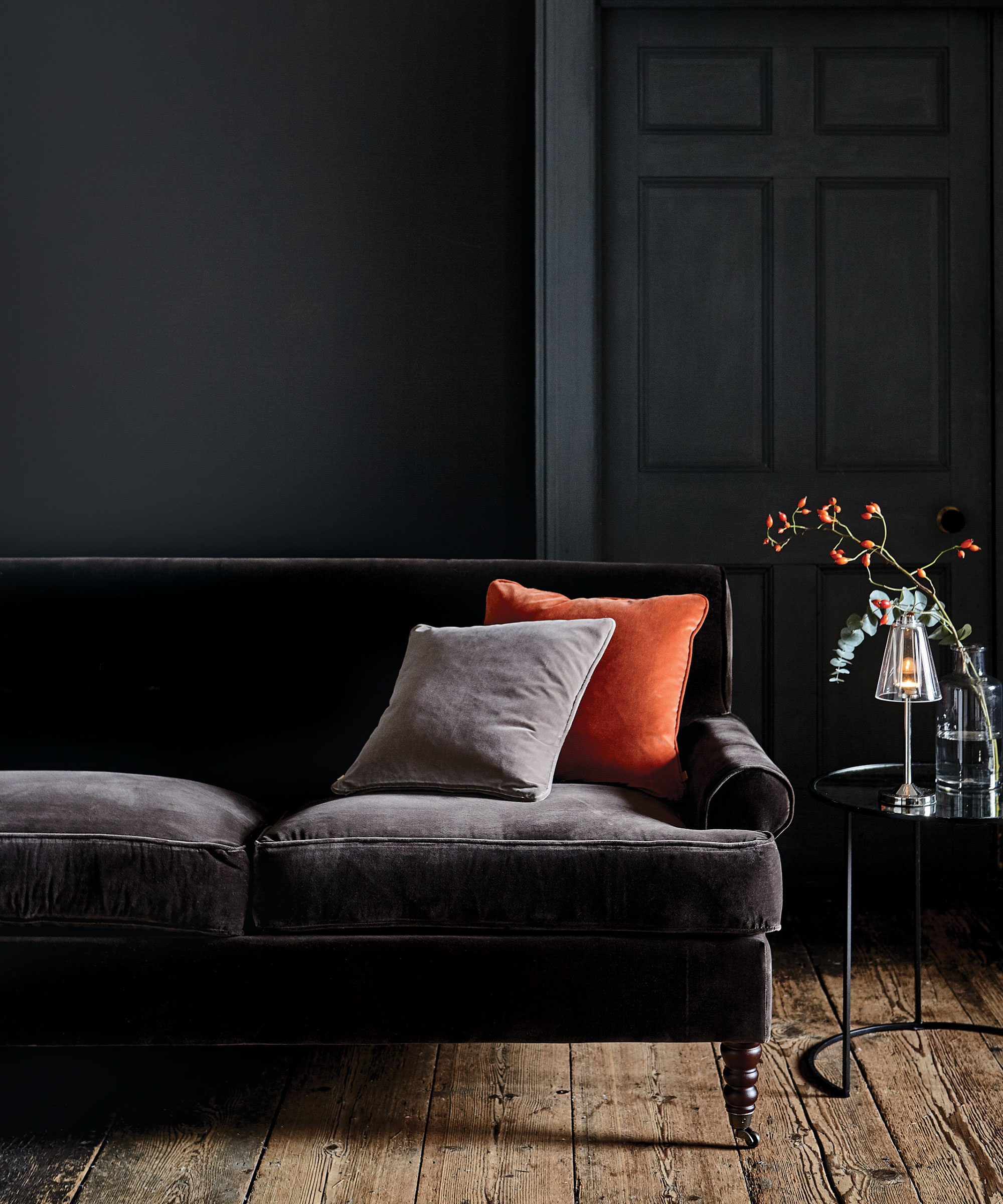 A rich, black living room with velvet sofa and rustic wooden floorboards.