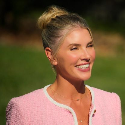 amanda kloots wears a pink suit and her hair in a bun smiling in the netflix reality show let's marry harry