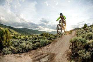 A female mountain biker wearing a helmet goes down a dirt hill in Colorado on a sunny day