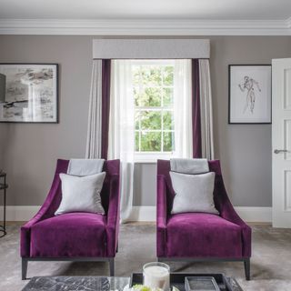 grey living room with grey and purple curtains and two single purple sofas with grey pillows