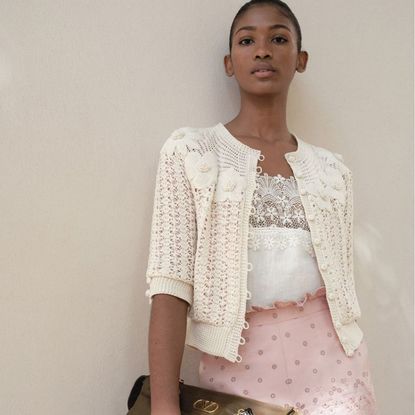 photo of young woman wearing Valentino bag, pink skirt, and white blouse.