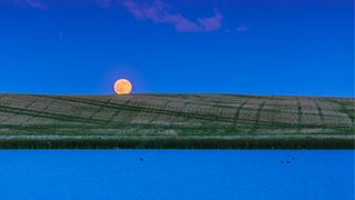 The full moon rising over fields and water in Canada.
